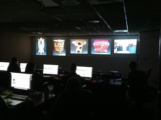 An image of a past Artist Image Review Workshop. Images are projected side by side horizontally and jurors sit at computers reviewing the images.