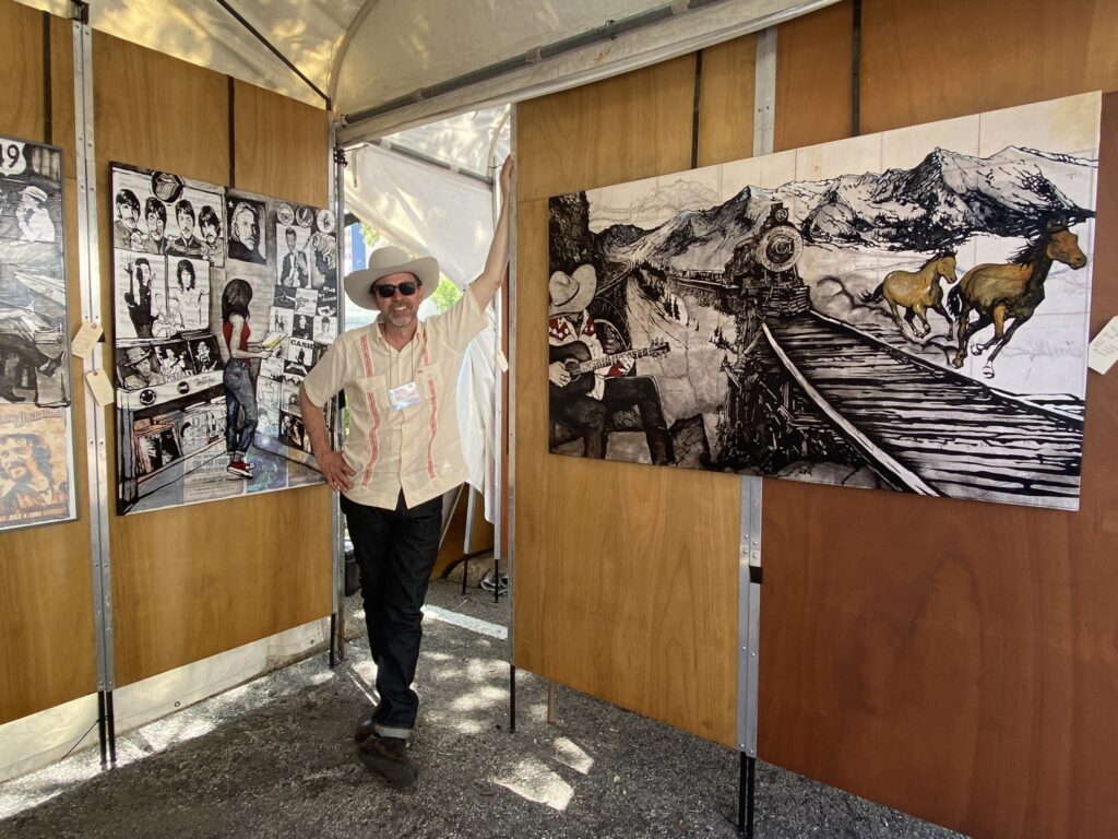 Photo of Will Armstrong standing inside of a booth at a art festival displaying his artwork.